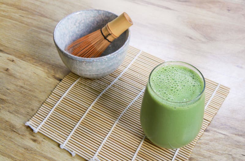 Matcha Green Tea Smoothie with Stone Bowl and wooden whisk on bamboo mat on table