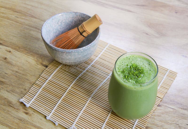 Matcha Green Tea Smoothie with Stone Bowl and wooden whisk on bamboo mat on table