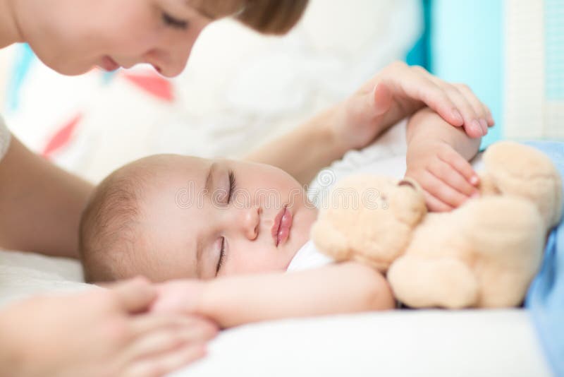 maternidad paternidad Madre joven que mira a su bebé que duerme en cama fotos de archivo libres de regalías maternidad paternidad Madre joven que mira a su bebé que duerme en cama fotos de archivo libres de regalías