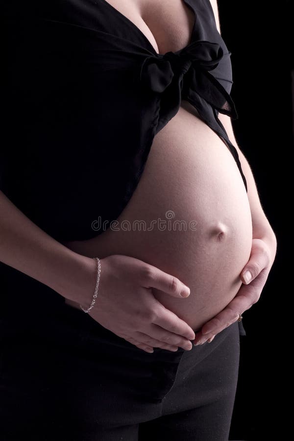 Close up studio shot of a pregnant maternity belly on black background. Close up studio shot of a pregnant maternity belly on black background