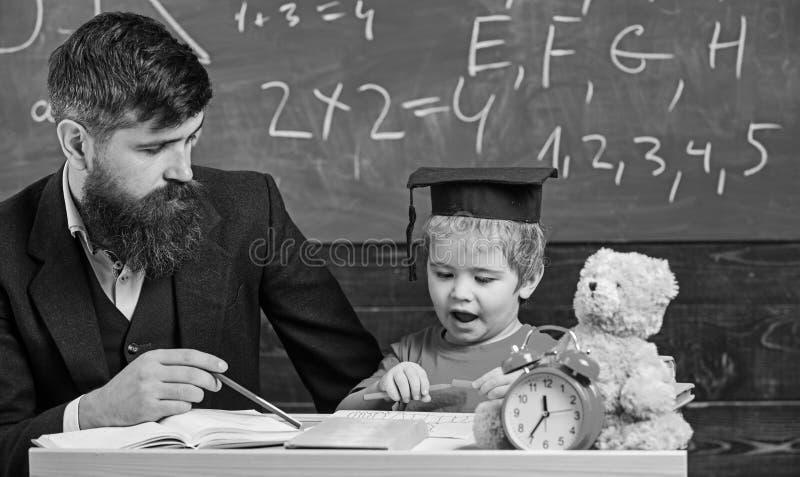 Mathematics Lesson Concept. Father Teaches Son Mathematics. Teacher In Formal Wear And Pupil In Mortarboard In Classroom