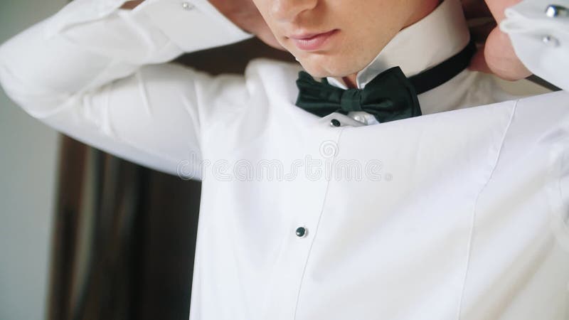 Matin du marié attachant un lien sur une chemise blanche.