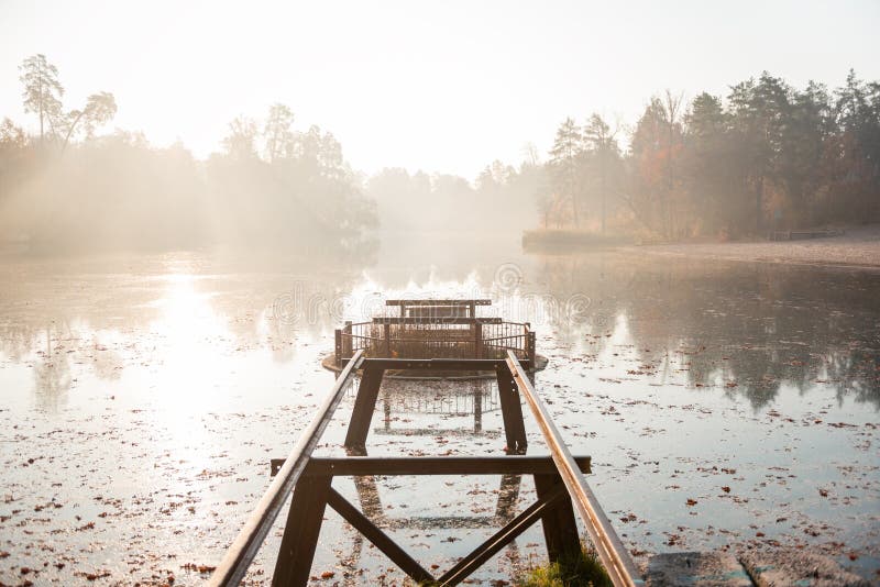 Matin sur le lac. Rails métalliques menant à une déversoir ronde. forêt couverte de brouillard en arrière-plan eau calme reflétant les arbres.