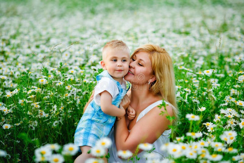Matka bawi się ze swoim blondynem na polu kwitnienia stokrotki. cieszyć się zapachem bukietu rumianków fotografia stock