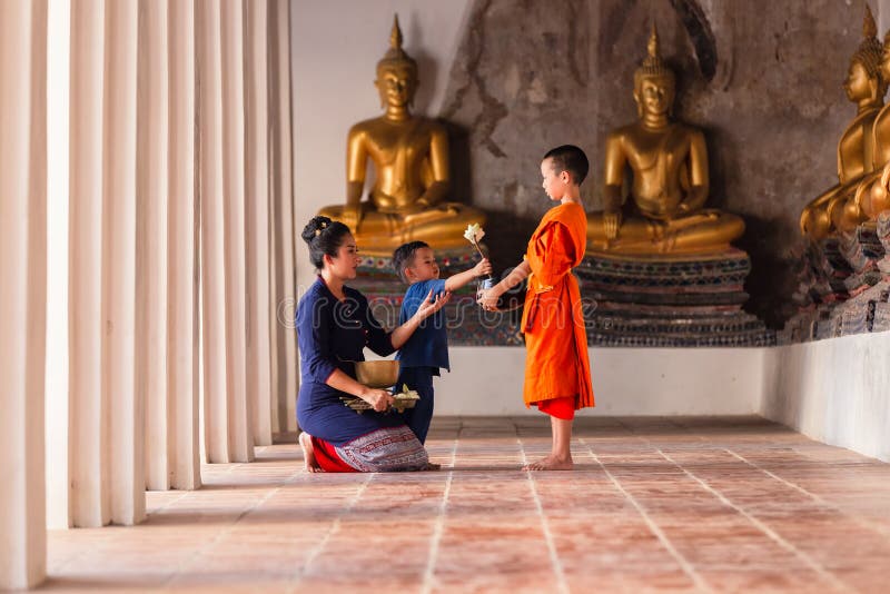 Mother and child family Thai Buddhists are giving alms to novices making merit with monk in Wat Phutthai Sawan Temple, Ayutthaya, Thailand. Mother and child family Thai Buddhists are giving alms to novices making merit with monk in Wat Phutthai Sawan Temple, Ayutthaya, Thailand