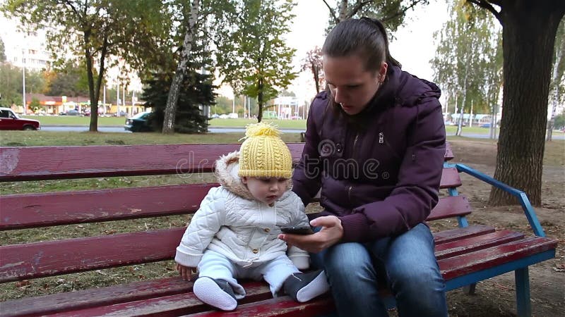 Matka z dziecka obsiadaniem na parkowej ławce Mama pokazuje twój dziecku smartphone