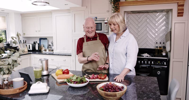 Matkock och lyckligt äldre par i köket vid matlagning av mat. Näringsriktig maträtt för middag och lagarbete stock video