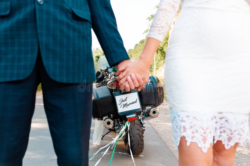 Matrimonio, sposi novelli Un uomo e una donna in abiti da sposa si tengono le mani l'un l'altro Sullo sfondo, c'è una motociclett fotografia stock libera da diritti Matrimonio, sposi novelli Un uomo e una donna in abiti da sposa si tengono le mani l'un l'altro Sullo sfondo, c'è una motociclett fotografia stock libera da diritti