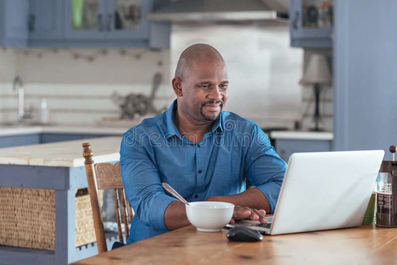 Mature African man browsing online with a laptop over breakfast