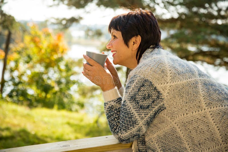 Mature attractive woman standing on terrace with cup of hot coffee royalty free stock photography Mature attractive woman standing on terrace with cup of hot coffee royalty free stock photography