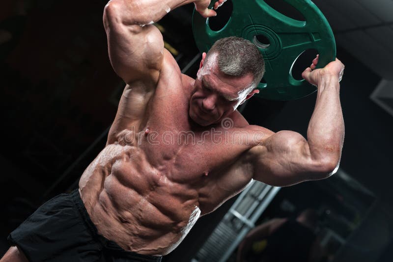 Mature bodybuilder posing with heavy weight in gym