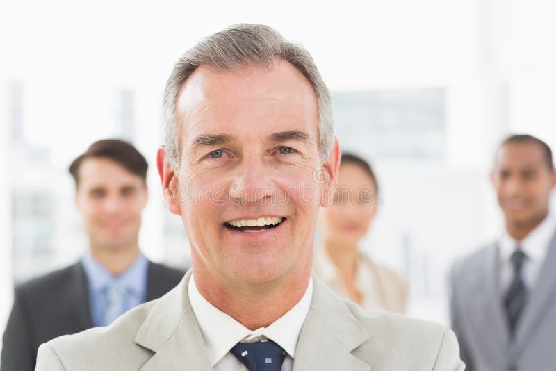 Mature businessman smiling at camera with team behind him