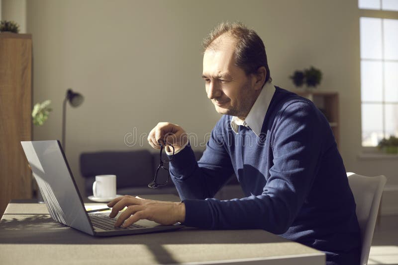 Mature businessman working on laptop sitting at desk in his home office in the morning royalty free stock image