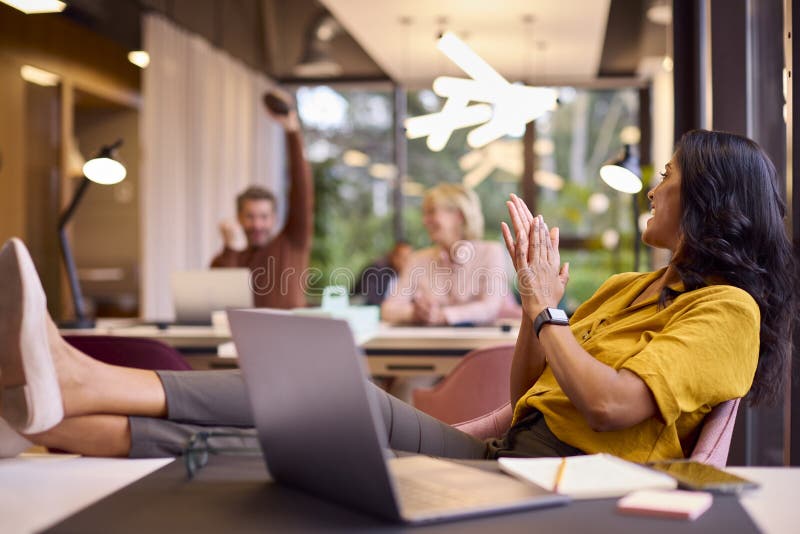 Mature Businesswoman With Feet On Desk In Office Throwing Small American Football