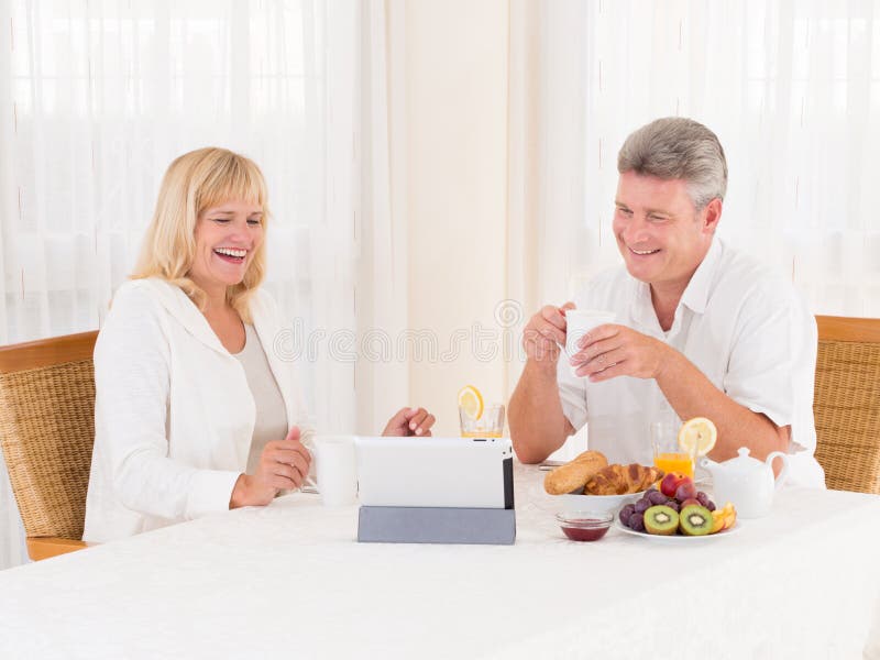 Mature couple laughing and video chatting with a tablet as they eat healty breakfast royalty free stock photo Mature couple laughing and video chatting with a tablet as they eat healty breakfast royalty free stock photo