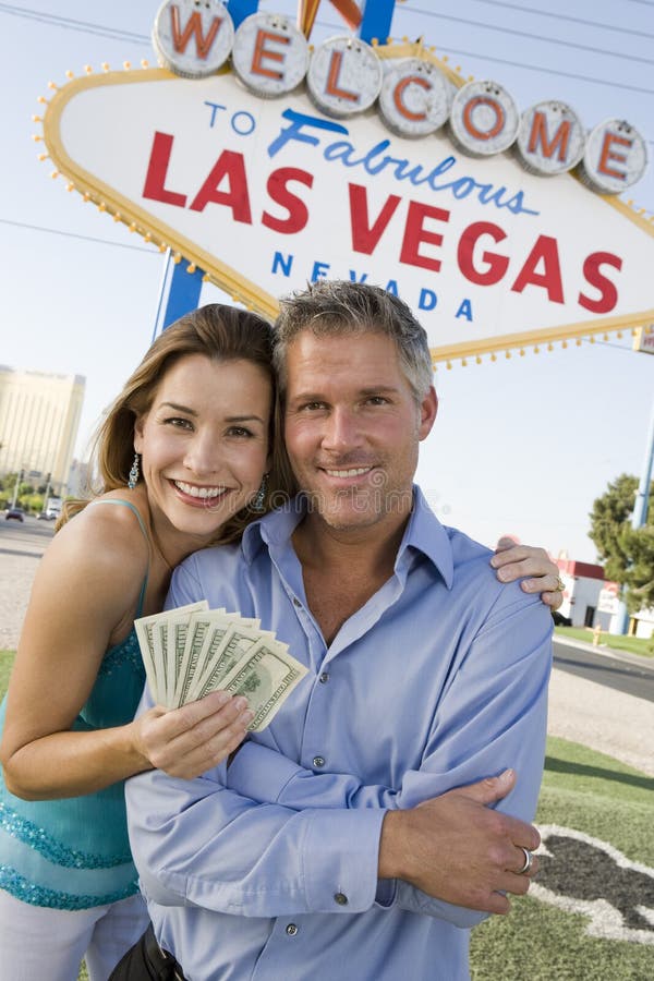Portrait of happy mature couple with money and welcome sign in the background