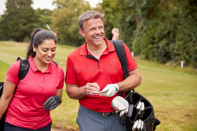 Mature Couple Playing Round Of Golf Carrying Golf Bags And Marking Scorecard