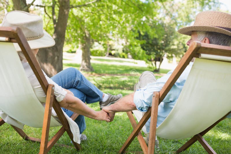 Mature couple sitting in deck chairs at park. Rear view of a relaxed mature couple sitting in deck chairs at the park royalty free stock photography Mature couple sitting in deck chairs at park. Rear view of a relaxed mature couple sitting in deck chairs at the park royalty free stock photography