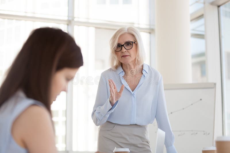 Mature female boss scolding intern for bad work results close up