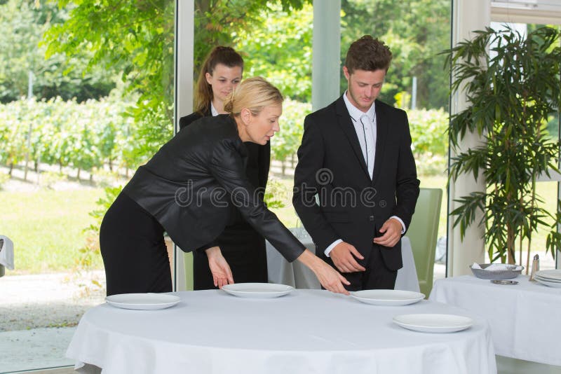 Mature hotel manager showing waiters how to properly set table stock images