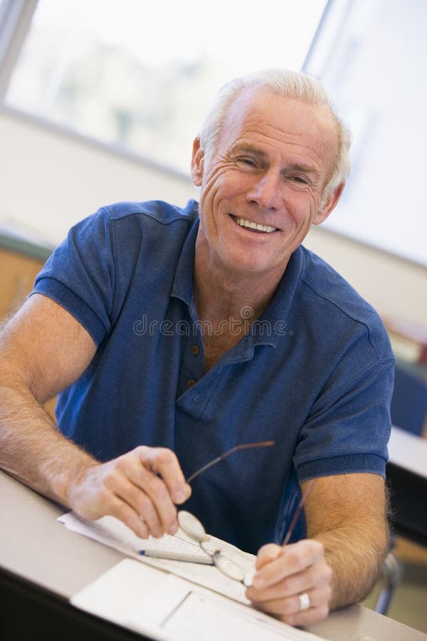 Mature male student holding glasses in class