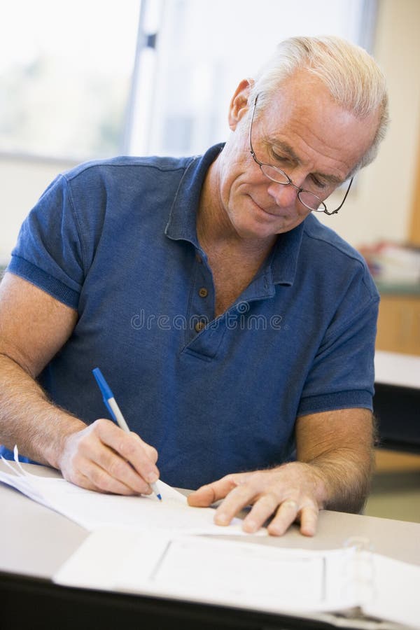 Mature male student writing in class stock image