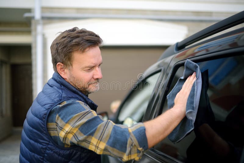 A mature man cleans his car with rag. Driver washes the glass of his car using microfiber washcloth. Father prepares the car for a family trip to nature