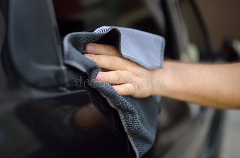 A mature man cleans his car with rag. Driver washes the glass of his car using microfiber washcloth. Father prepares the car for a family trip to nature