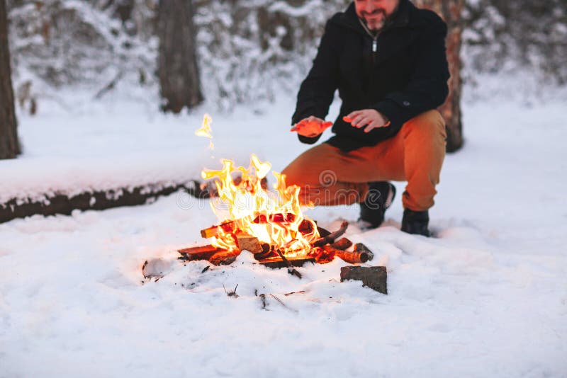 Mature man warming his hands with campfire in snowy forest