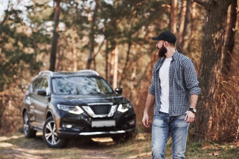 Mature mec a une promenade Homme barbu près de sa toute nouvelle voiture noire dans le concept de vacances en forêt image libre de droits Mature mec a une promenade Homme barbu près de sa toute nouvelle voiture noire dans le concept de vacances en forêt image libre de droits