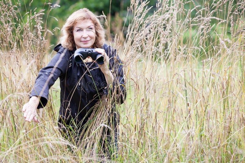 Mature woman with binoculars in high grass, bird watcher, copy space