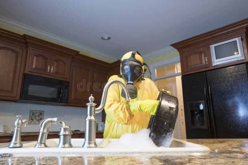 Mature woman in Haz Mat suit washing pot in kitchen sink