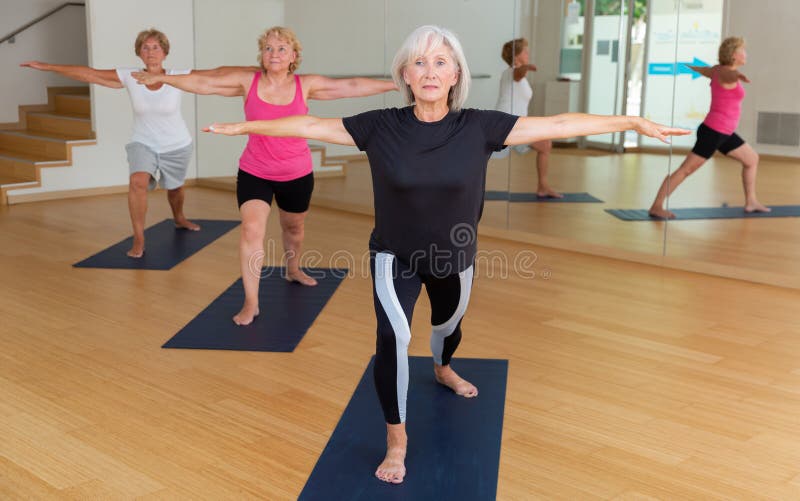 Portrait of sporty mature woman practicing Virabhadrasana known as Warrior Pose during group yoga training. Portrait of sporty mature woman practicing Virabhadrasana known as Warrior Pose during group yoga training.