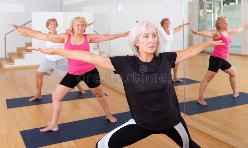 Portrait of sporty mature woman practicing Virabhadrasana known as Warrior Pose during group yoga training. Portrait of sporty mature woman practicing Virabhadrasana known as Warrior Pose during group yoga training.