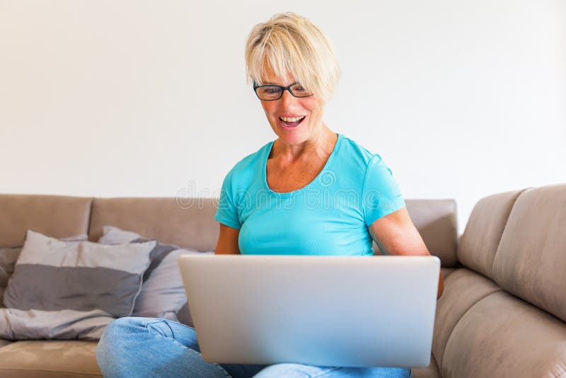 Mature woman sits who is rejoicing with raised hands in front of a laptop