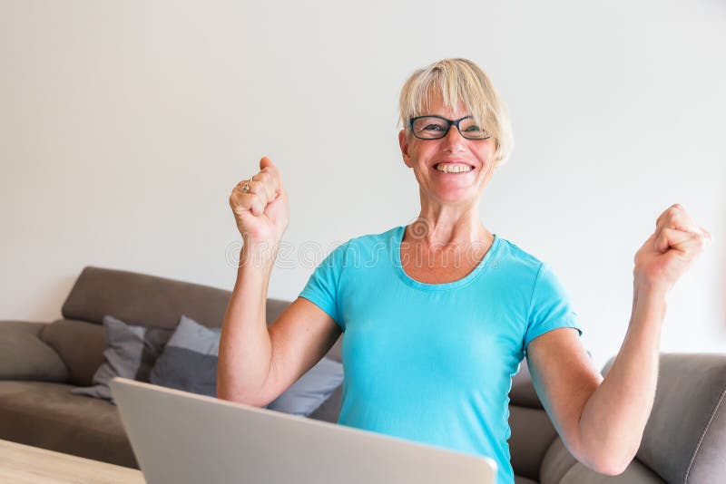 Mature woman sits who is rejoicing with raised hands in front of a laptop