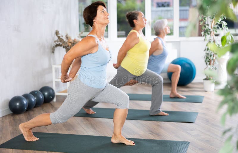Group of elderly female people are practicing Hatha yoga for amateurs. Mature women stands in warrior pose, Virabhadrasana. Group of elderly female people are practicing Hatha yoga for amateurs. Mature women stands in warrior pose, Virabhadrasana