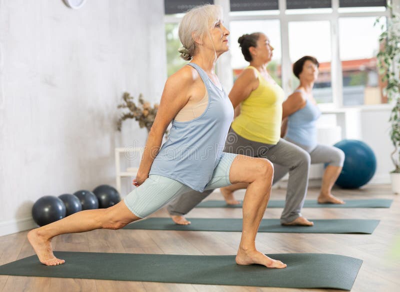 Group of elderly female people are practicing Hatha yoga for amateurs. Mature women stands in warrior pose, Virabhadrasana. Group of elderly female people are practicing Hatha yoga for amateurs. Mature women stands in warrior pose, Virabhadrasana