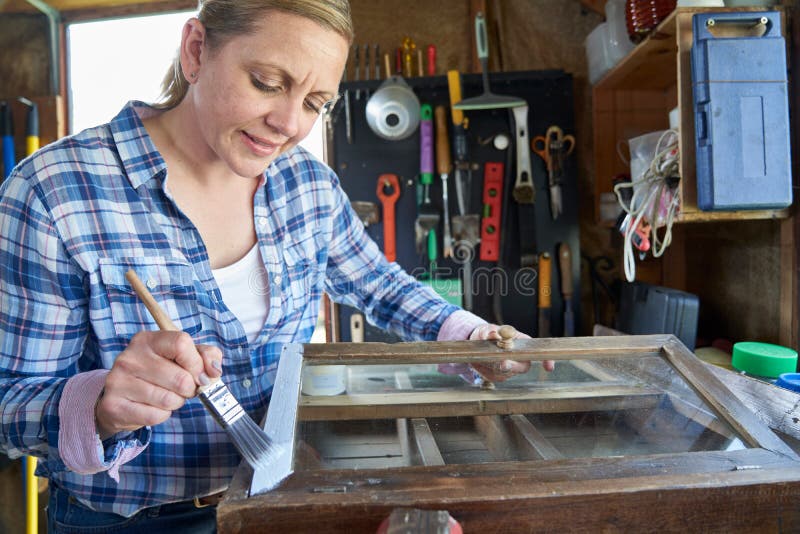 Mature Woman Upcycling Furniture In Workshop At Home  Painting Cabinet