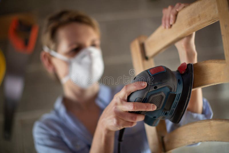 Mature Woman Upcycling Furniture In Workshop At Home Using Electric Sander