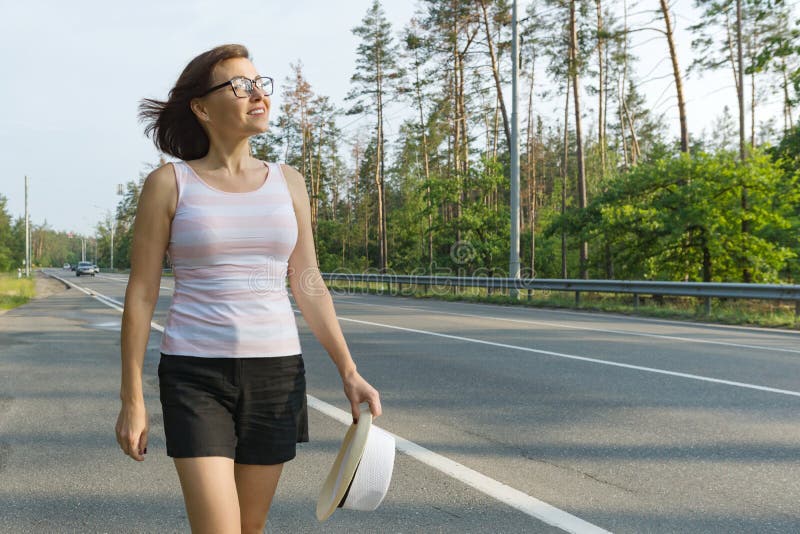 Mature woman walks along the road ahead, looks into the distance, copy spac...