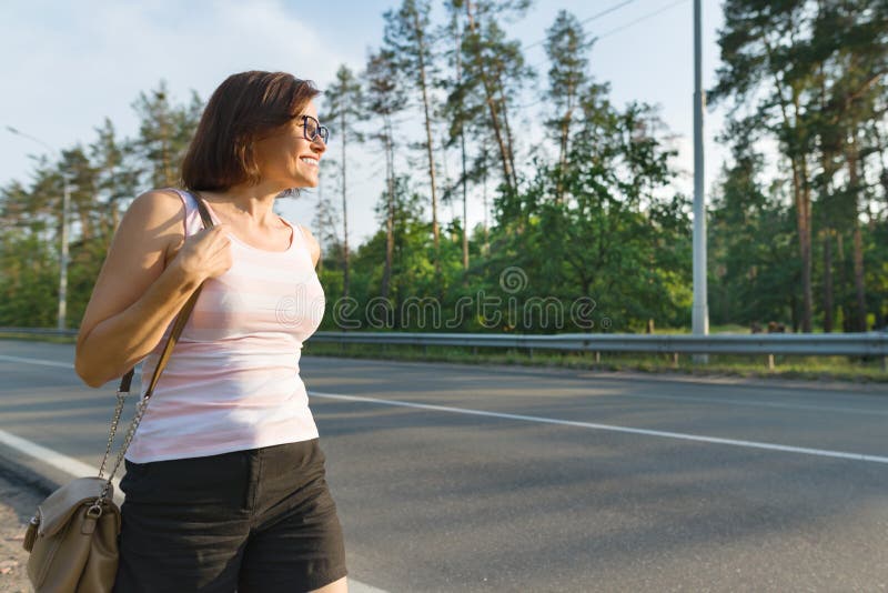 Mature woman walks along the road ahead, looks into the distance, copy spac...