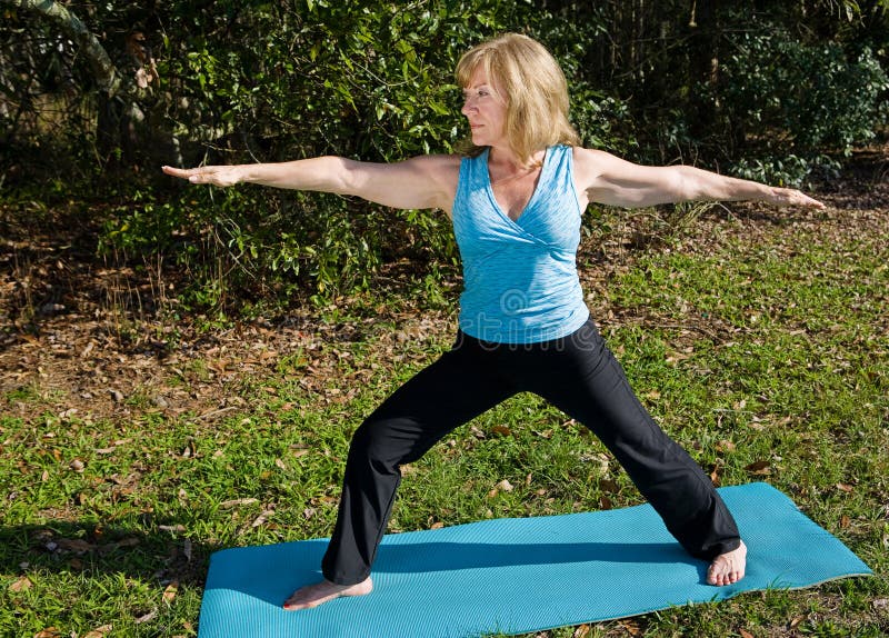 Beautiful sixty year old woman doing the warrior asana outdoors in a natural setting. Beautiful sixty year old woman doing the warrior asana outdoors in a natural setting.