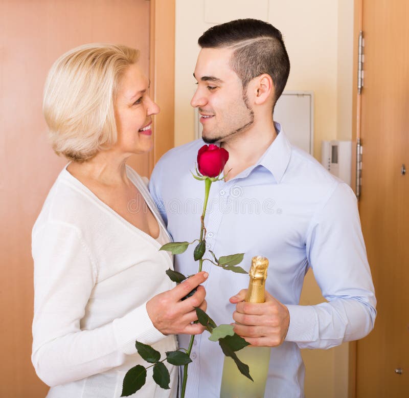 mature woman young guy doorway smiling elderly women meeting handsome boyfriend flowers wine hands 68939259