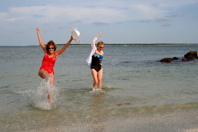 Zwei ältere Damen im Badeanzug am Strand planschen im Meer.