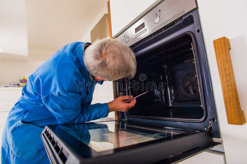 Mature workman fixing oven stock photo. Image of housework 135437630