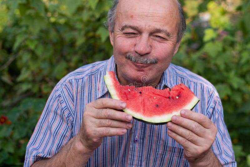 Maturi l'uomo caucasico con i baffi che mangia l'anguria succosa con piacere e sorridere fotografie stock libere da diritti Maturi l'uomo caucasico con i baffi che mangia l'anguria succosa con piacere e sorridere fotografie stock libere da diritti