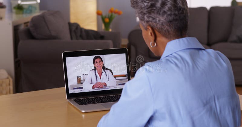 Maturi la donna africana che parla con medico sul computer portatile immagine stock libera da diritti Maturi la donna africana che parla con medico sul computer portatile immagine stock libera da diritti
