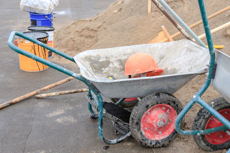 Matériaux de construction et une brouette avec un casque sur une surface foncée photos libres de droits Matériaux de construction et une brouette avec un casque sur une surface foncée photos libres de droits