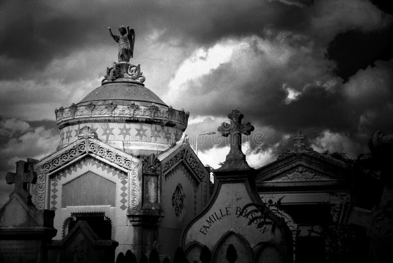 Black and white image of a stone mausoleum and tombstones iin an ancient cemetery in France. Image has photo grain effect added. Black and white image of a stone mausoleum and tombstones iin an ancient cemetery in France. Image has photo grain effect added.